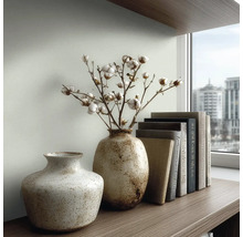 Twee gespikkelde keramische vazen met gedroogde katoentakken en een rij boeken op een houten plank voor een raam.