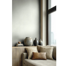 Moderne woonkamer met lichtgrijze muur, houten dressoir met decoratieve vazen en een bank met diverse kussens naast een groot raam.