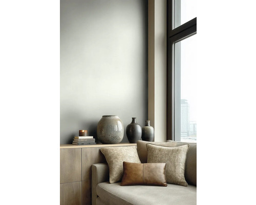 Moderne woonkamer met lichtgrijze muur, houten dressoir met decoratieve vazen en een bank met diverse kussens naast een groot raam.