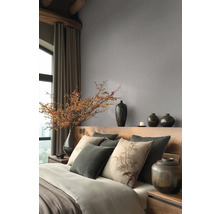 Moderne slaapkamer met grijs vliesbehang, houten hoofdbord, kussens met boommotief en decoratieve donkere vazen.