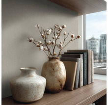 Twee gestructureerde keramieken vazen op een houten plank, één met katoentakken, naast een stapel boeken voor een muur met textuur.