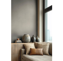 Modern ingerichte woonkamer met een wand in mat taupe achter een houten dressoir met vazen en een bank naast een raam.