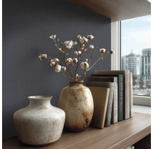 Gestructureerd behang in donkerblauw achter twee keramieken vazen met katoentakken en boeken op een houten plank in een modern, georganiseerd design.