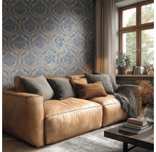 Lichte woonkamer met blauw-beige damastbehang achter een bruine leren bank met kussens en een houten raam.