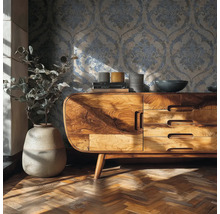 Woonkamer met behang met ornamenten, dressoir van massief hout, vaas met plant en visgraatparket.