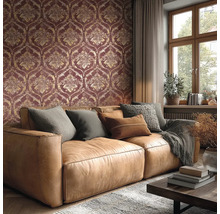 Woonkamer met behang in damastpatroon in donkerrood en goud, bruine leren bank met kussens en een raam.
