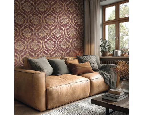 Woonkamer met behang in damastpatroon in donkerrood en goud, bruine leren bank met kussens en een raam.