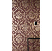 Vliesbehang met barok damastpatroon in goudlook op rode achtergrond, met een gouden tafellamp op een donkere tafel.