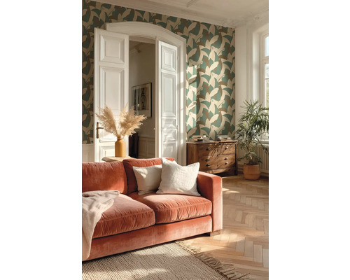 Woonkamer met vliesbehang met bladmotief, fluwelen bank, visgraatparket en houten ladekast in een lichte omgeving.