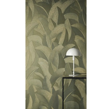 Vliesbehang met gestructureerd patroon van tropische bladeren. Een witte tafellamp op een zwarte tafel staat voor de muur.