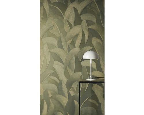 Vliesbehang met gestructureerd patroon van tropische bladeren. Een witte tafellamp op een zwarte tafel staat voor de muur.