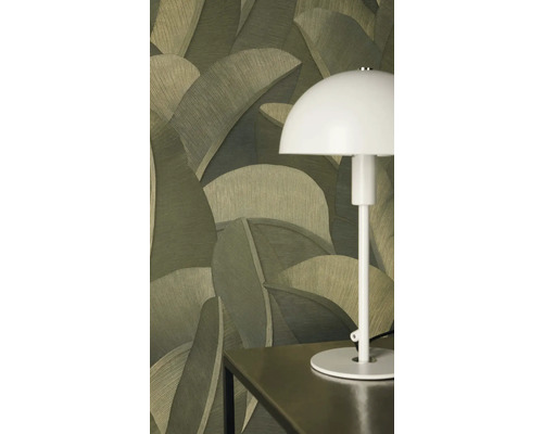 Vliesbehang met groot palmbladmotief in verschillende groentinten achter een witte tafellamp op een donkere tafel.