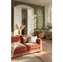 Woonkamer met groen behang met bladmotief, terracotta fluwelen bank en visgraatparket in helder licht.