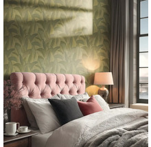 Een gezellige slaapkamer met groen behang met bladpatroon, een roze gecapitonneerd hoofdbord en warme verlichting van een tafellamp.