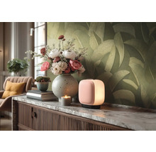 Moderne, kubusvormige tafellamp met zacht licht op een dressoir met marmeren blad, boeket bloemen in vaas en behang met bladmotief.