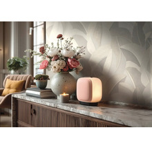 Licht vliesbehang met bladmotief in de woonkamer achter een dressoir met bloemenvaas en kleine lamp.