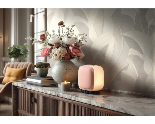 Licht vliesbehang met bladmotief in de woonkamer achter een dressoir met bloemenvaas en kleine lamp.