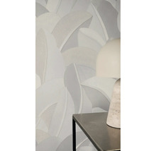 Vliesbehang met groot, gestructureerd bladpatroon in neutrale grijstinten op een muur achter een moderne tafellamp.