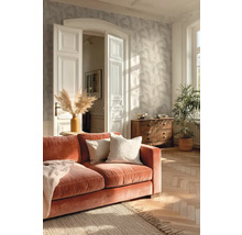 Lichte woonkamer met behang met bladmotief, visgraatparket, oranje fluwelen bank en een houten ladekast.