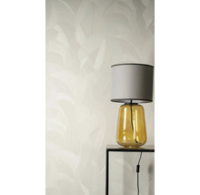 Vliesbehang met een subtiel bladerpatroon achter een tafellamp met gele glazen voet en grijze stoffen kap op een zwarte bijzettafel.