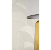 Vliesbehang met bladpatroon en textuur in lichtbeige naast een tafellamp.