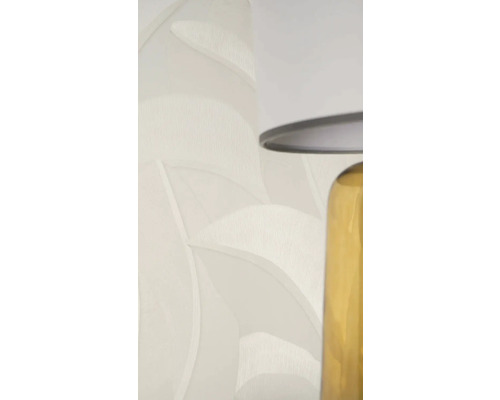 Vliesbehang met bladpatroon en textuur in lichtbeige naast een tafellamp.