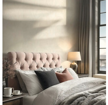 Lichte slaapkamer met gecapitonneerd hoofdbord, beddengoed met textuur, een tafellamp en schaduwen van zonlicht op de muur.