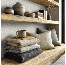 Gestructureerde wandbekleding in een lichte kamer met houten planken, aardewerk, gevouwen dekens en kussens in een moderne natuurlijke stijl.