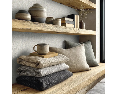 Gestructureerde wandbekleding in een lichte kamer met houten planken, aardewerk, gevouwen dekens en kussens in een moderne natuurlijke stijl.