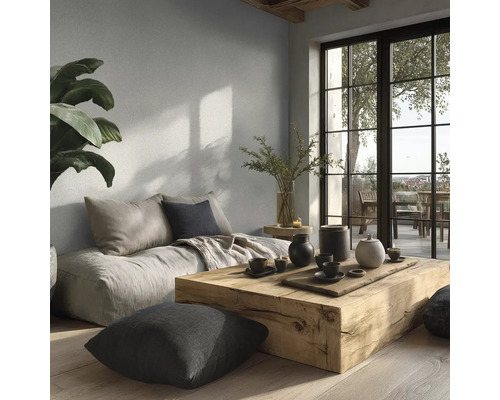 Moderne woonkamer met lichtgrijze muurverf, massief houten tafel, vloerkussens en grote raampartij naar het balkon.