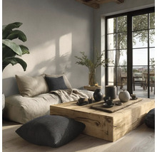 Lichte woonkamer met massieve houten tafel, lage vloerbank, kussens en grote ramen in minimalistische stijl met natuurlijke wandafwerking.