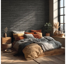 Slaapkamer met wandafwerking in steenlook, houten bed, textiel in aardetinten en helder daglicht door een raam.