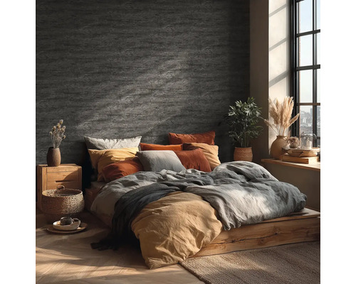 Slaapkamer met wandafwerking in steenlook, houten bed, textiel in aardetinten en helder daglicht door een raam.