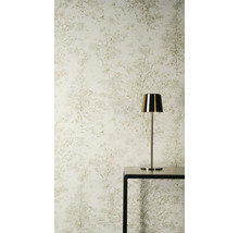 Vliesbehang met subtiel boompatroon en bosmotief in lichte tinten achter een gouden tafellamp op een zwarte tafel.