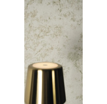 Licht behang met subtiel botanisch takkenpatroon in een getextureerde look achter een glanzende metalen lamp.