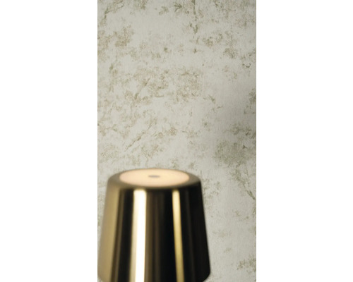 Licht behang met subtiel botanisch takkenpatroon in een getextureerde look achter een glanzende metalen lamp.