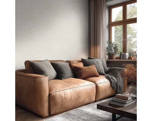 Lichtgekleurd behang met subtiele textuur op de wand achter een bruine leren bank in een gezellige woonkamer met raam.