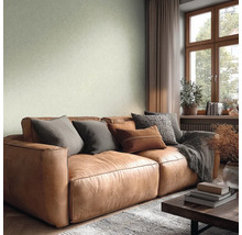 Woonkamer met lichtgroen structuurbehang, een bruine leren bank met kussens, houten raamkozijn en een lichte, gezellige sfeer.