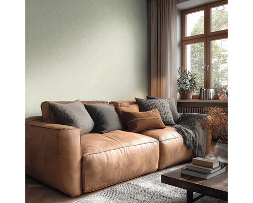 Woonkamer met lichtgroen structuurbehang, een bruine leren bank met kussens, houten raamkozijn en een lichte, gezellige sfeer.