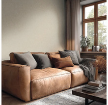 Gezellige woonkamer met bruine leren bank, kussens, beige structuurbehang en houten raam.