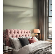 Lichte slaapkamer met een roze gecapitonneerd hoofdbord, lichtgroene muurverf, comfortabel beddengoed en een tafellamp.