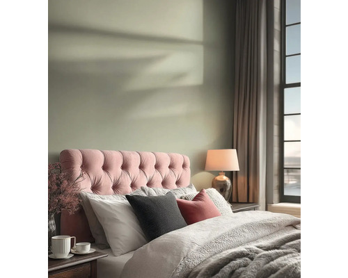 Lichte slaapkamer met een roze gecapitonneerd hoofdbord, lichtgroene muurverf, comfortabel beddengoed en een tafellamp.