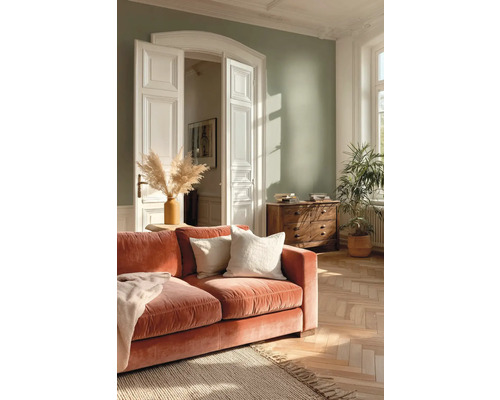 Lichte woonkamer met saliegroene muur, terracotta fluwelen bank, houten dressoir, visgraatparket en een grote kamerplant.