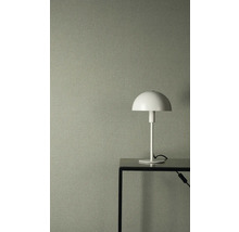 Gestructureerd vliesbehang in grijsgroen met linnenlook, gecombineerd met een witte tafellamp op een zwarte metalen tafel.