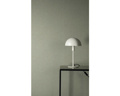 Gestructureerd vliesbehang in grijsgroen met linnenlook, gecombineerd met een witte tafellamp op een zwarte metalen tafel.