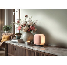 Moderne draagbare tafellamp met roze voorkant en wit licht op een marmeren dressoir naast een bloemenvaas en een kaars.