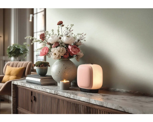 Moderne draagbare tafellamp met roze voorkant en wit licht op een marmeren dressoir naast een bloemenvaas en een kaars.