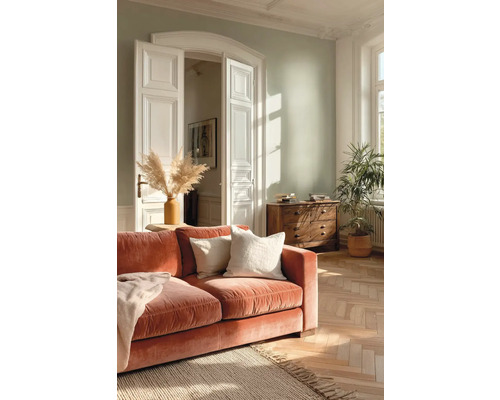 Lichte woonkamer met lichtgroene muur, roestkleurige fluwelen bank, visgraatparket, jute vloerkleed en witte dubbele deur.