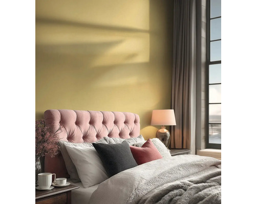 Lichte slaapkamer met gele muur, roze gecapitonneerd hoofdbord, grijs beddengoed en een nachtlampje naast een groot raam.