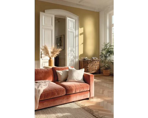 Lichte woonkamer met okergele muur, oranje fluwelen bank, visgraatparket, witte openslaande deuren en houten ladekast.